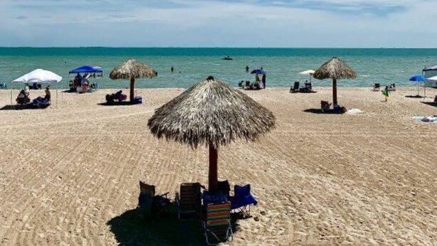 Ein Strand mit reetgedeckten Sonnenschirmen und Liegestühlen.