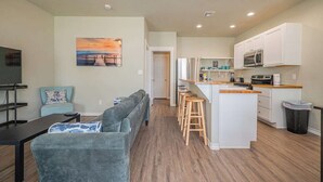Eine moderne Wohnung mit Wohnzimmer, einer Couch, einem Fernseher und einer Küche mit weißen Schränken sowie einem Holzboden.
