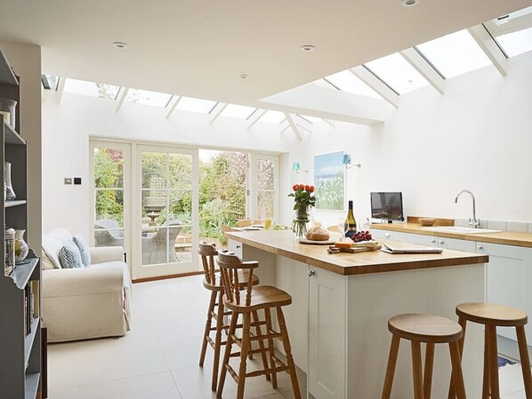 A modern kitchen with a large island, bar stools, and a dining area with a sofa and chairs.