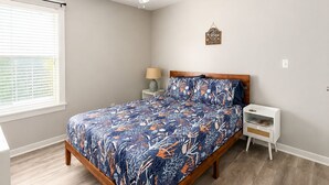 A bedroom with a bed, a nightstand, a lamp, a ceiling fan, and a window with blinds. - This cottage is a 2 bedroom(s), 2 bathrooms, located in Rockport, TX. (Rockport)