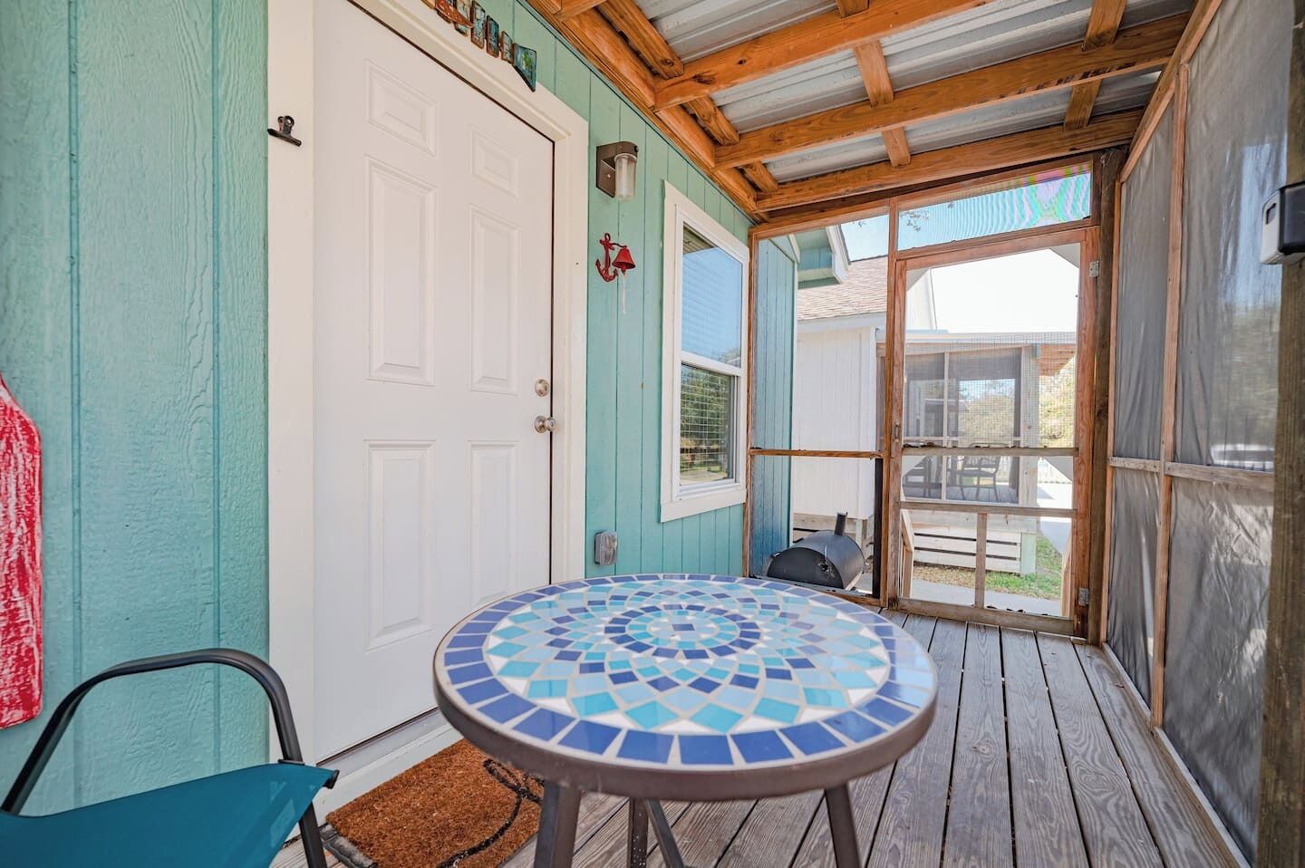 Une véranda avec une table à motifs de mosaïque, une porte et un barbecue.