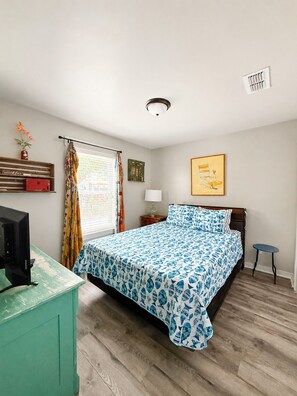 A bedroom with a bed, a desk, a lamp, a chair, and a window with curtains.