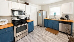 A modern kitchen with white and blue cabinetry, stainless steel appliances, and a wooden countertop. - This cottage is a 2 bedroom(s), 2 bathrooms, located in Rockport, TX. (Rockport)