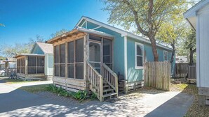 A single-story house with a covered porch, a small deck, and a wooden fence. - This cottage is a 2 bedroom(s), 2 bathrooms, located in Rockport, TX. (Rockport)