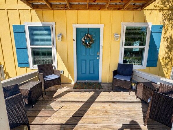 A wooden deck with wicker furniture, a blue door with a wreath, and shutters on windows.