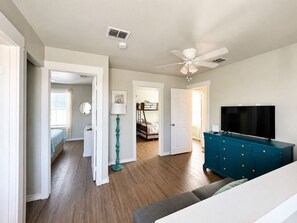 A room with a ceiling fan, a TV on a dresser, a bed with a blue blanket, and a floor lamp.