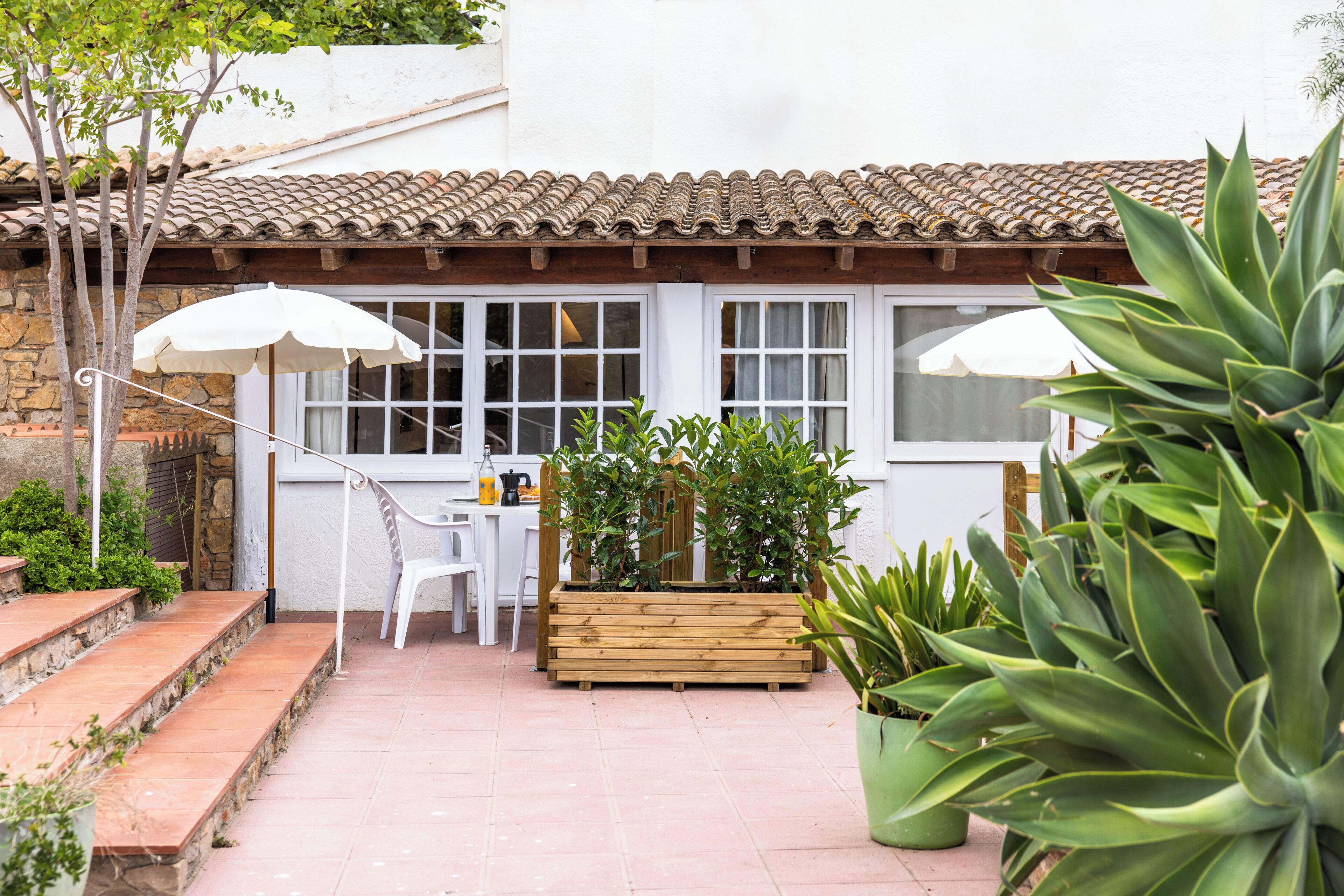 Un espace patio aménagé avec une table et des chaises en bois, deux parasols blancs et des plantes en pot.