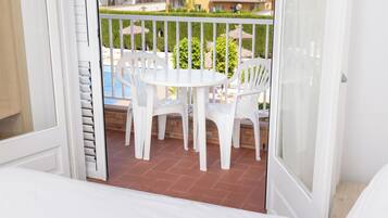 A balcony with a white table and chairs, a view of a swimming pool, and a brick floor.