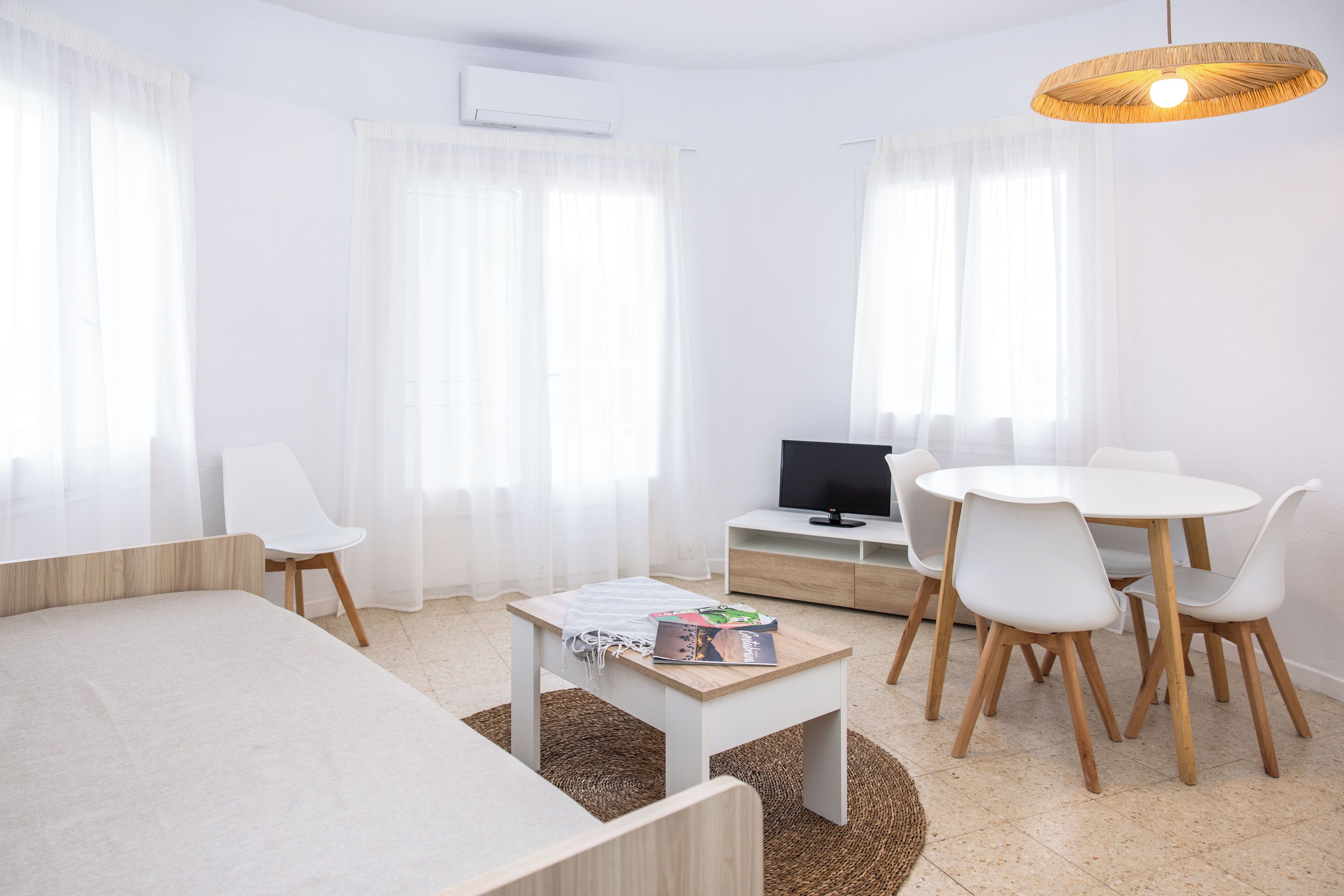 Een moderne, goed verlichte kamer met een bed, een klein tafeltje met boeken, een televisie en een zithoek met stoelen.