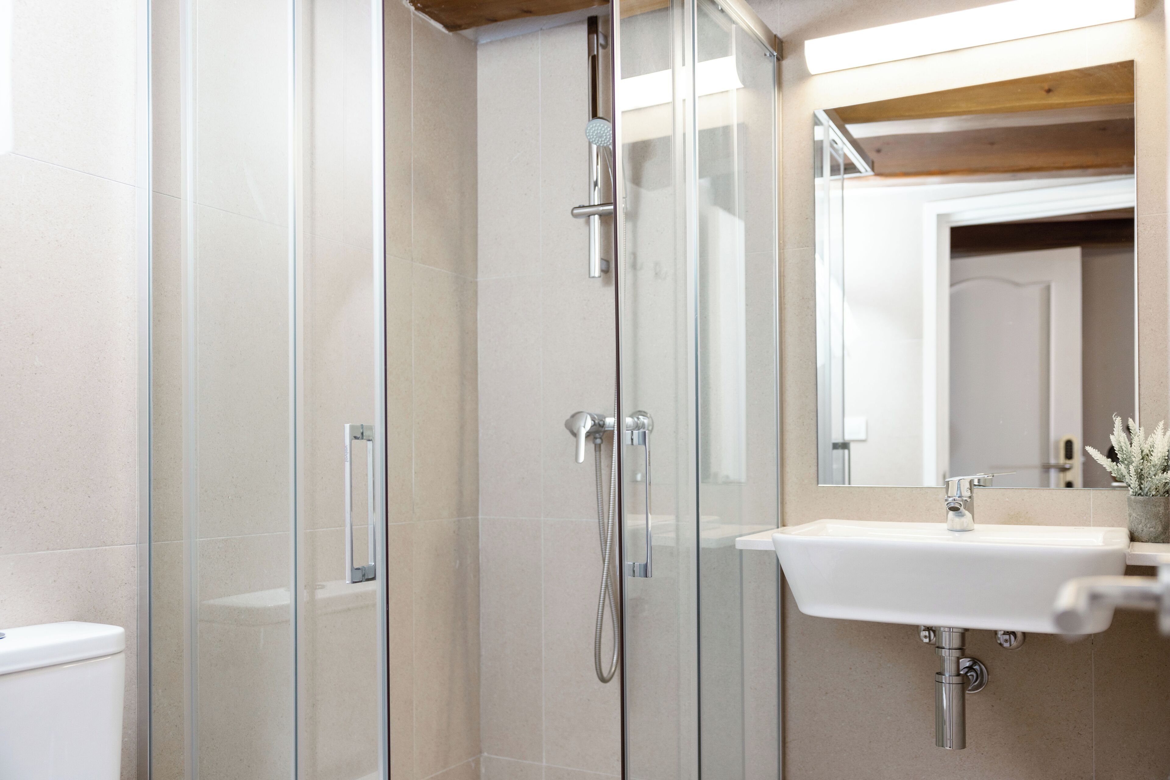 Un baño moderno con cabina de ducha de vidrio, un lavamanos blanco y un espejo sobre él.