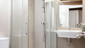 Un baño moderno con cabina de ducha de vidrio, un lavamanos blanco y un espejo sobre él.