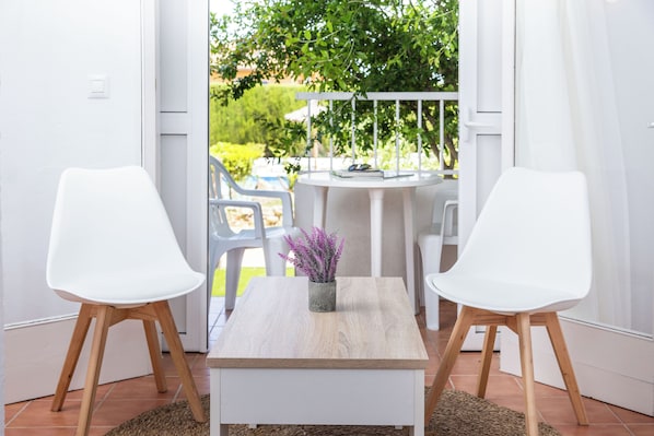 A modern room with a white table, two white chairs, a small potted plant, and a view of a garden through an open door. - RVApartaments Escala Brava (L'Escala)