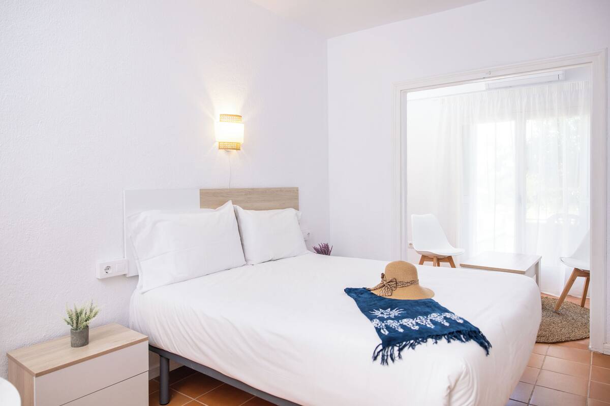 A neatly made bed with white linens, a wooden headboard, and a blue floral throw blanket.