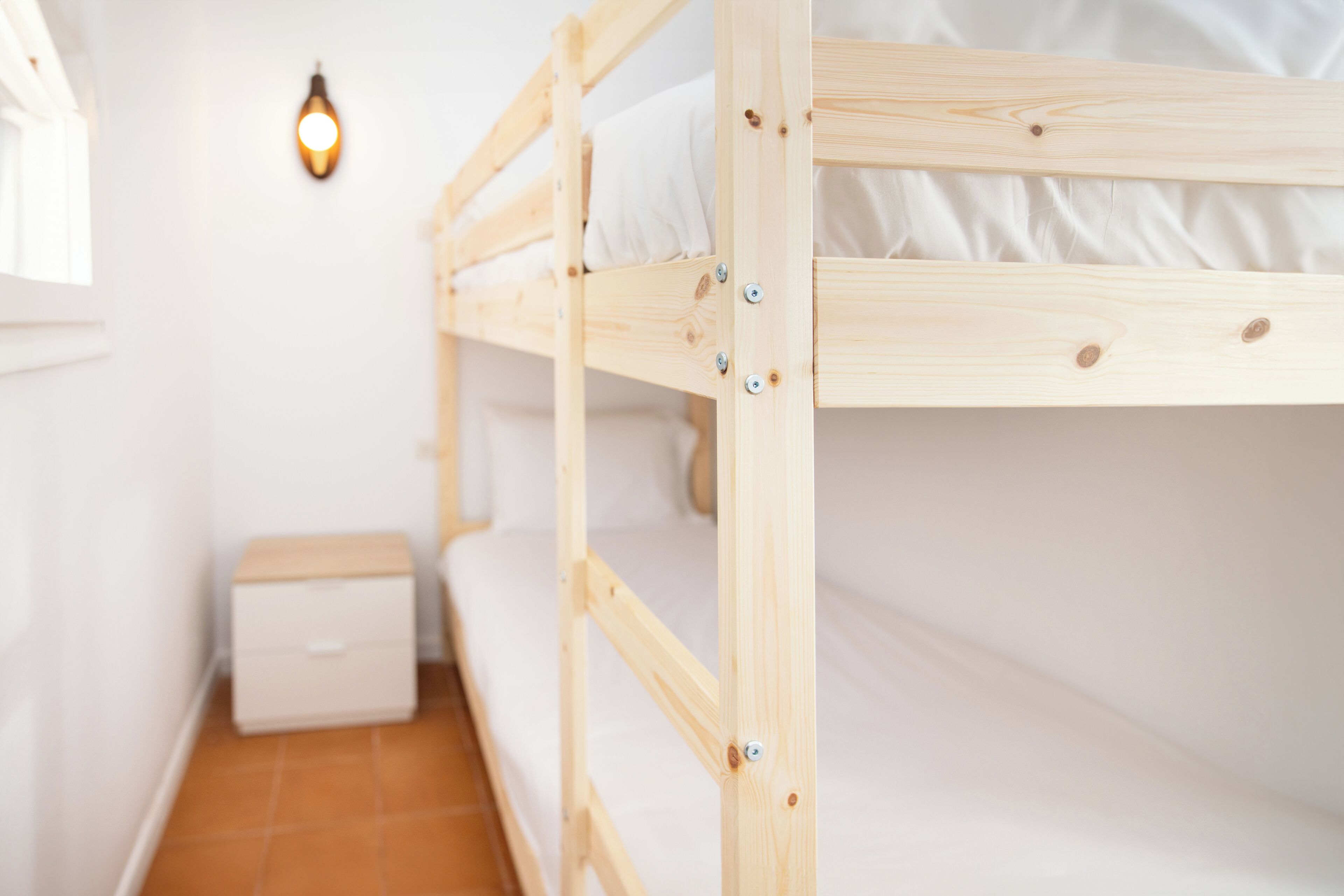 Een stapelbed met witte beddengoed en een klein nachtkastje.