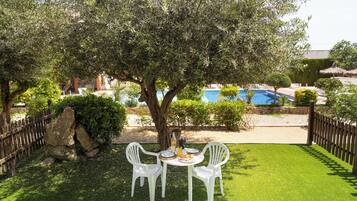 Un pati amb taula i cadires, un arbre i una piscina al fons.