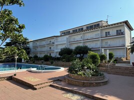 Un hotel de varios pisos con piscina, mobiliario exterior y un jardín ajardinado.
