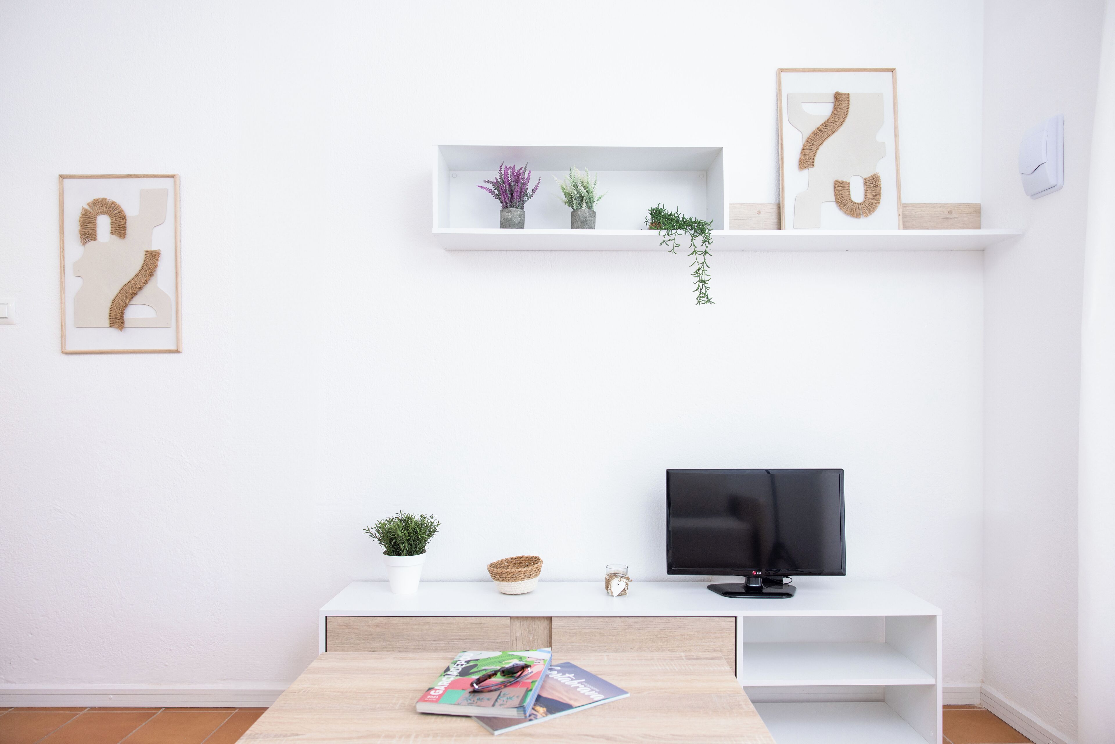 A modern living room with a white TV stand, a flat-screen TV, a magazine on the table, and two framed artworks on the wall.