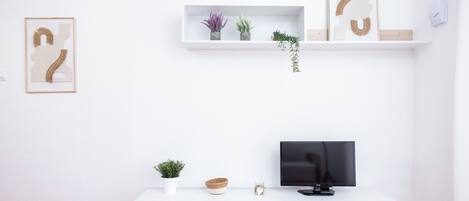 A modern living room with a white TV stand, a flat-screen TV, a magazine on the table, and two framed artworks on the wall.