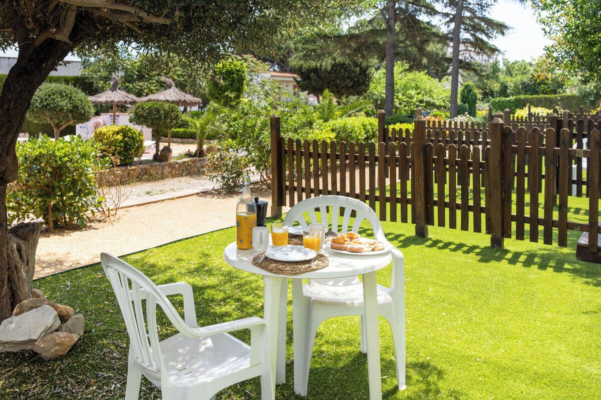 A white plastic table and chairs set on a grassy lawn with a wooden fence in the background.