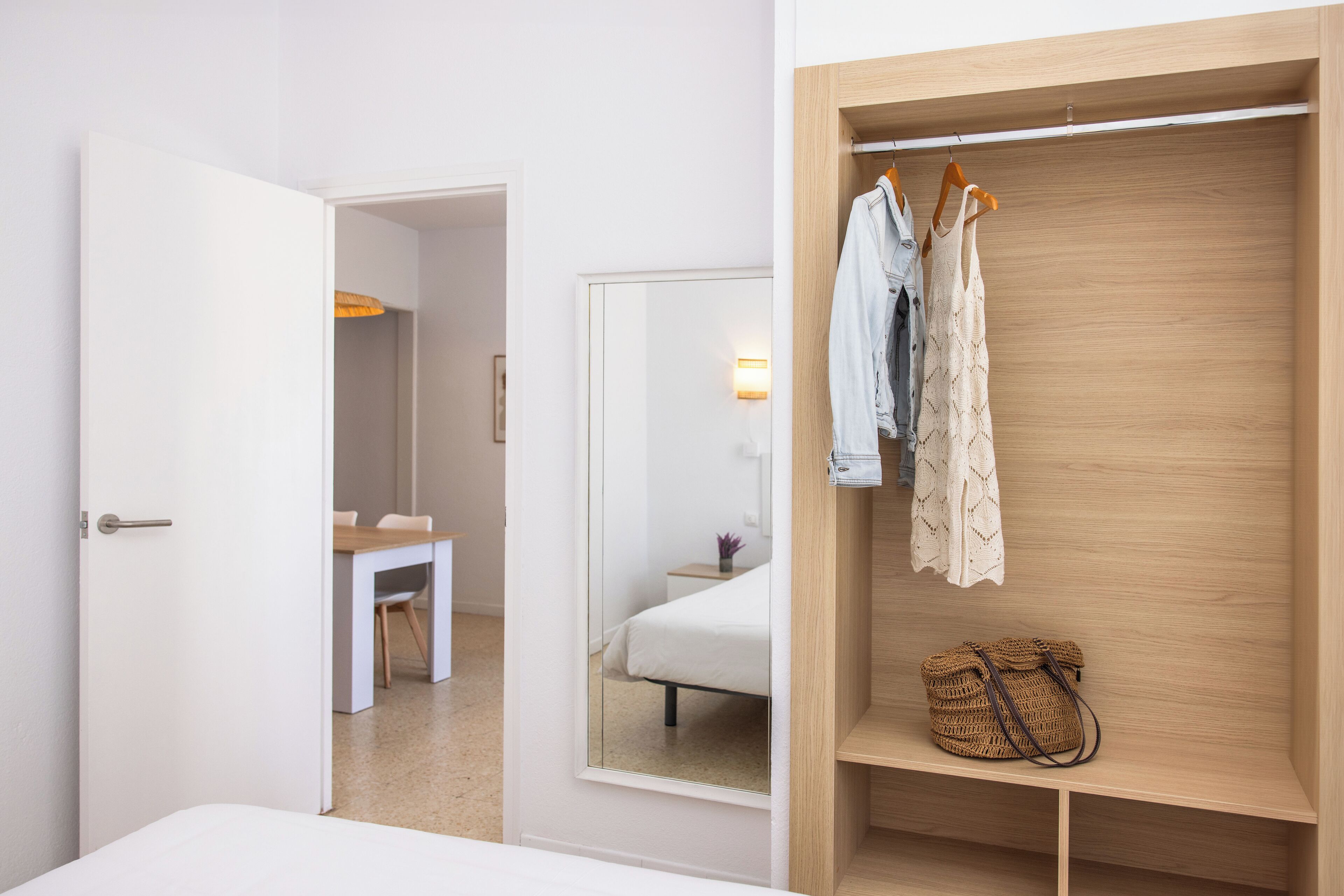 A hotel room with a wooden wardrobe, a bed, a desk, and a mirror.
