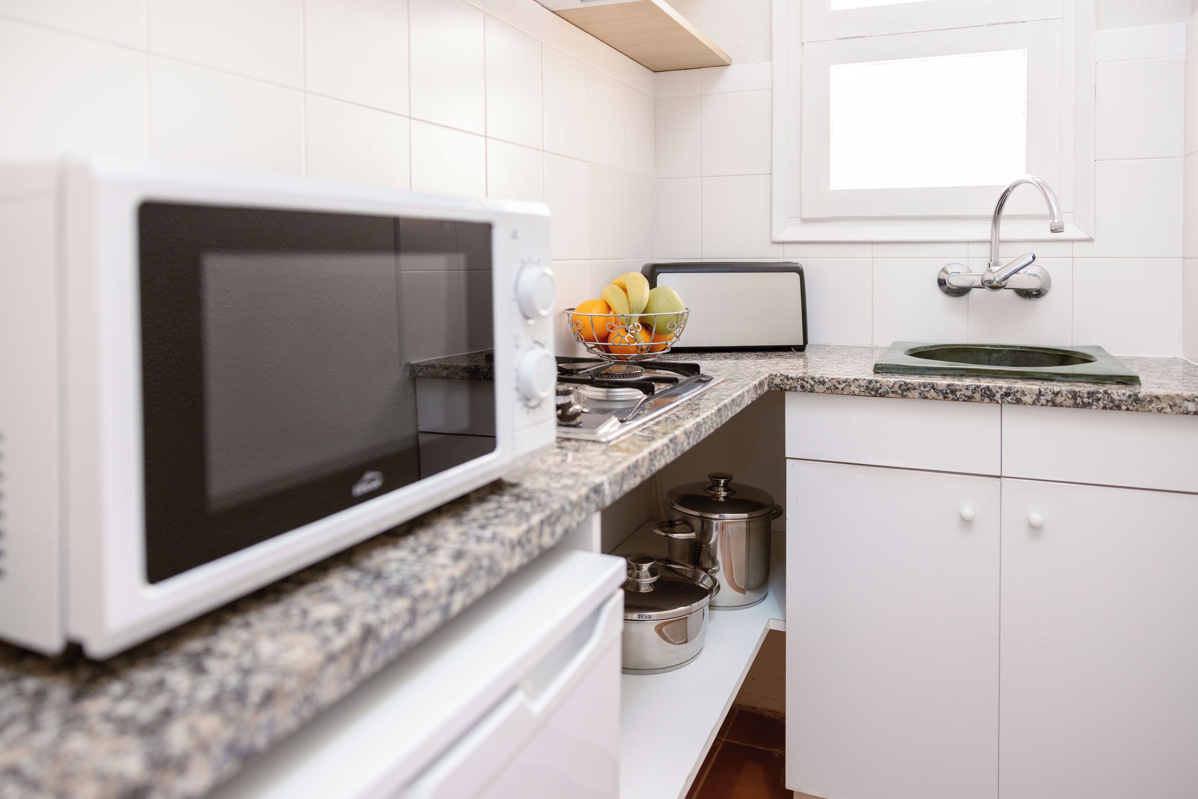 A kitchen with a white microwave, granite countertop, stainless steel pots, and a sink with a faucet.