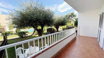 Un balcón con barandillas blancas, piso de baldosas y vistas a una piscina y árboles.