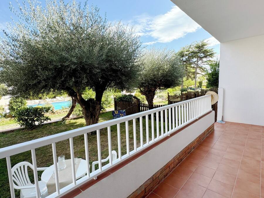 Un balcón con barandillas blancas, piso de baldosas y vistas a una piscina y árboles.