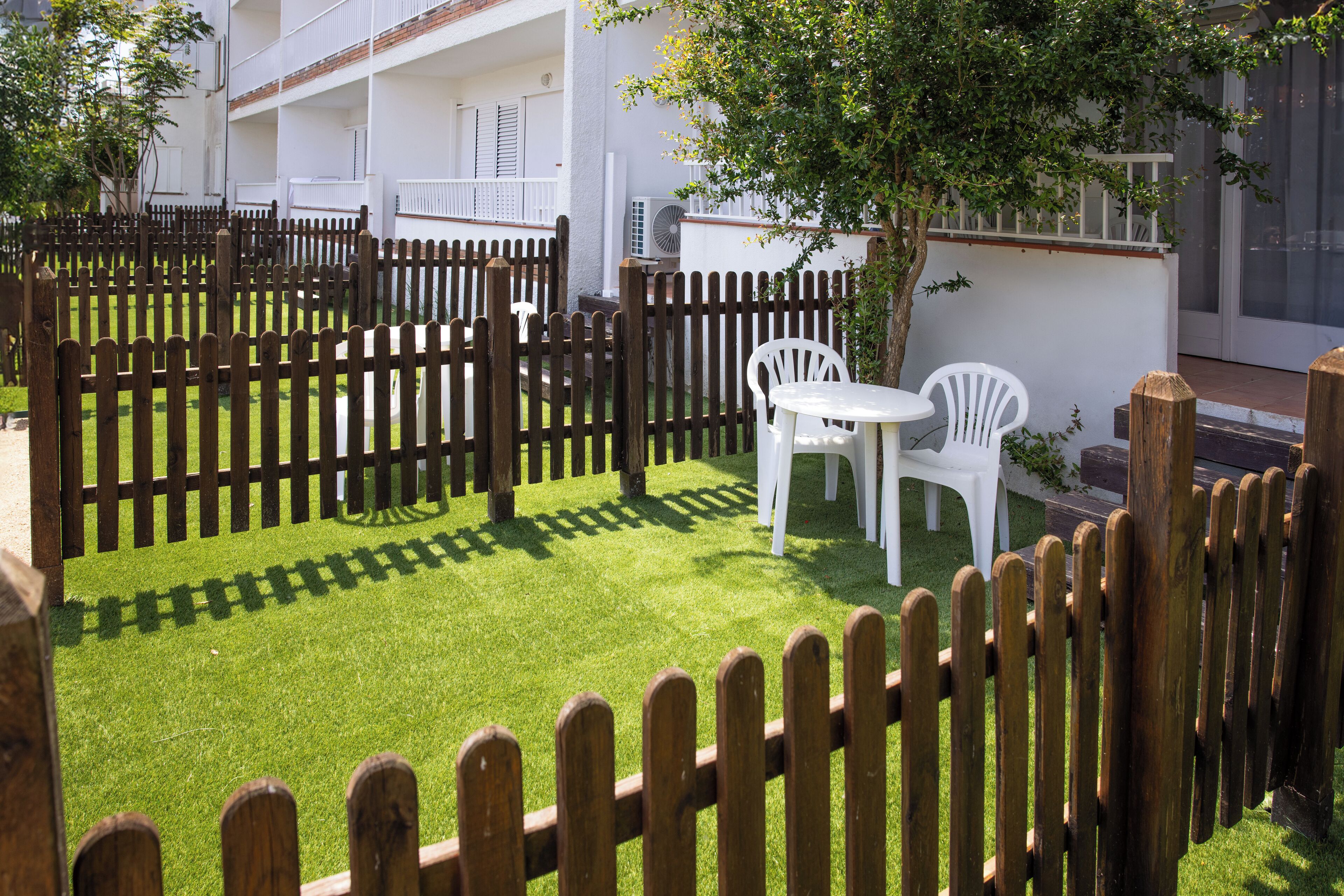 A fenced outdoor area with artificial grass, white plastic chairs, and a small table.