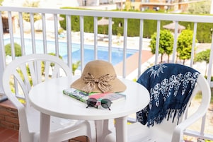 A white chair with a round table on a balcony overlooking a pool.