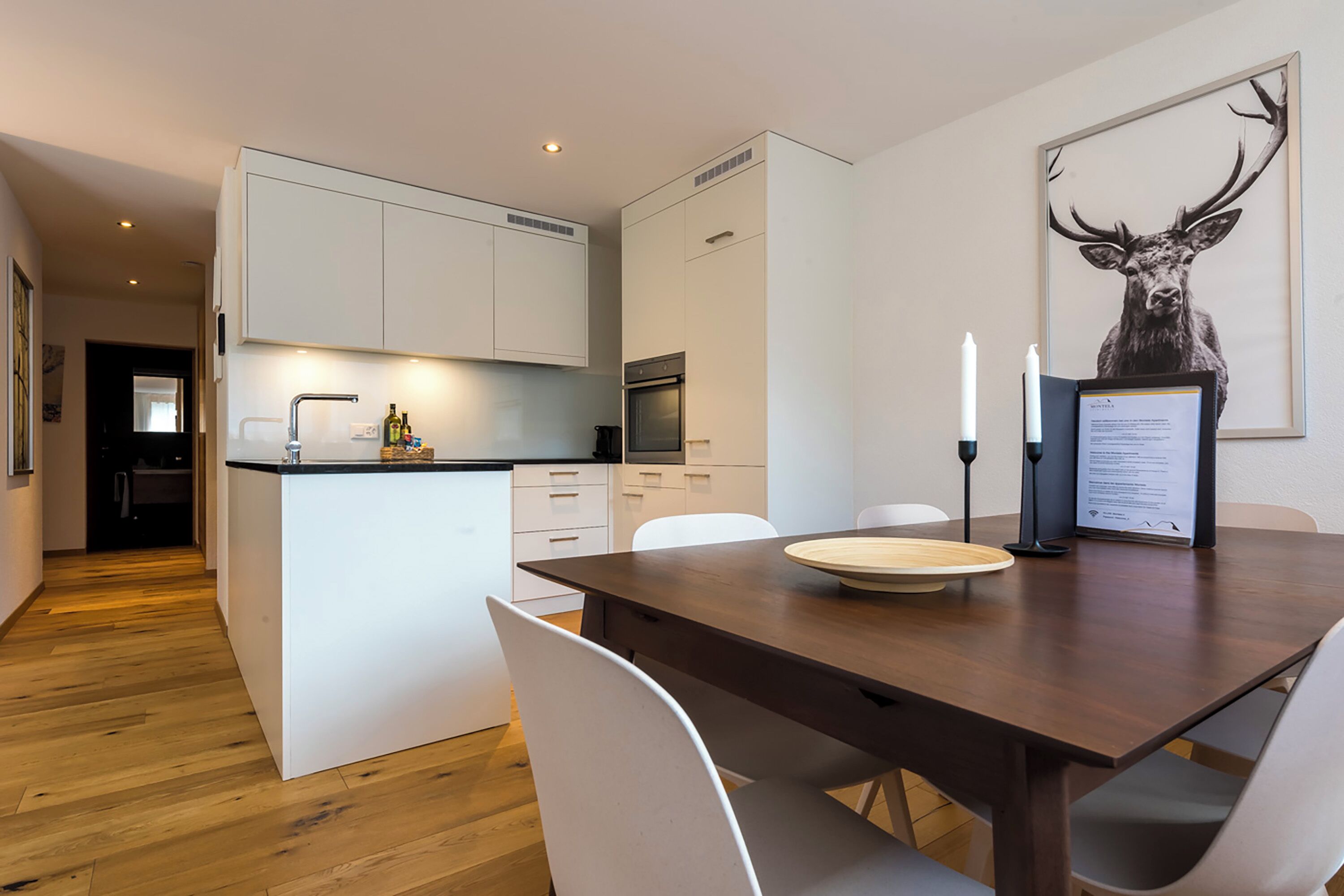 Una cocina moderna con armarios blancos, una mesa de comedor de madera y una obra de arte con un ciervo enmarcado.