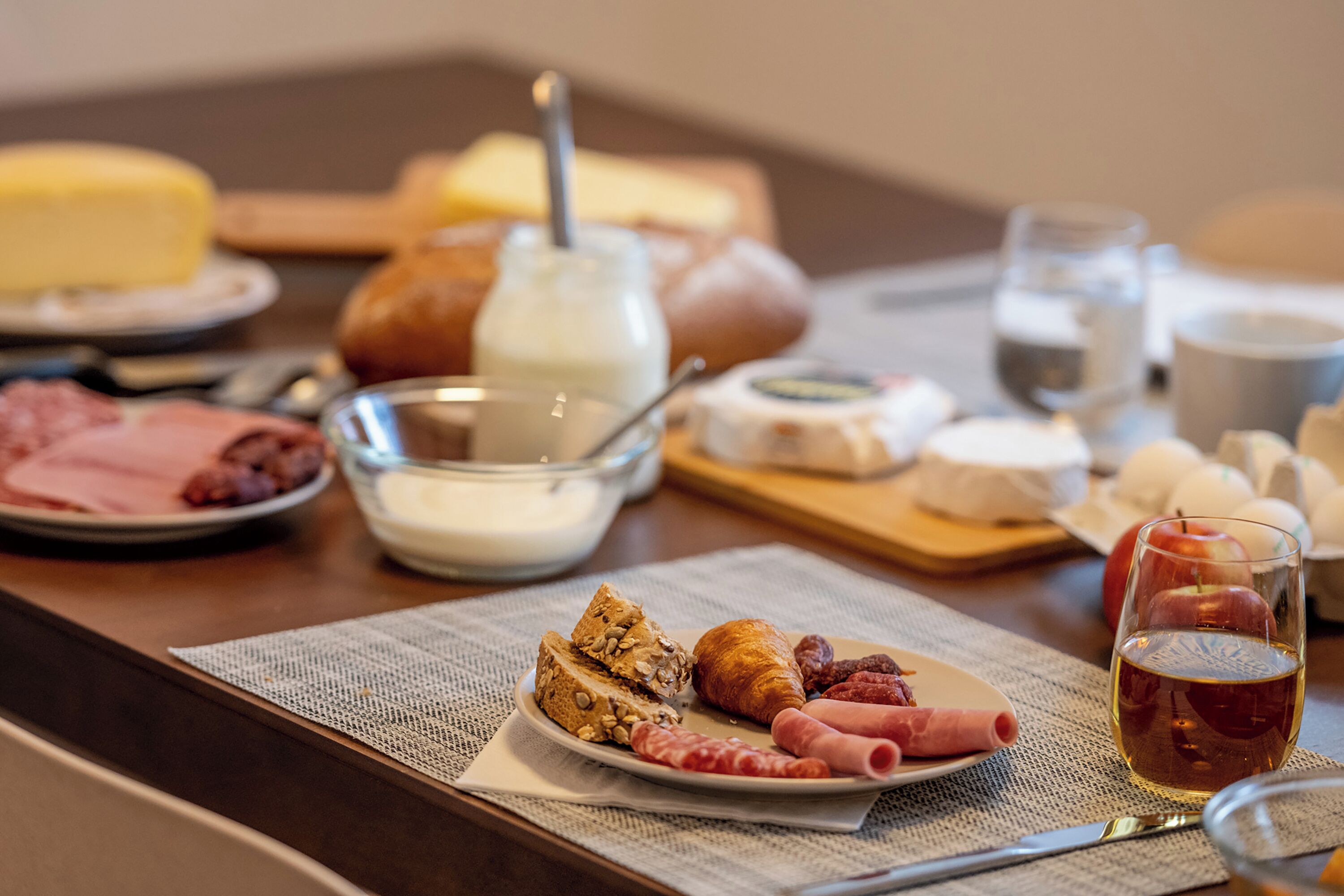 A breakfast table with various food items including bread, cheese, ham, and an apple.