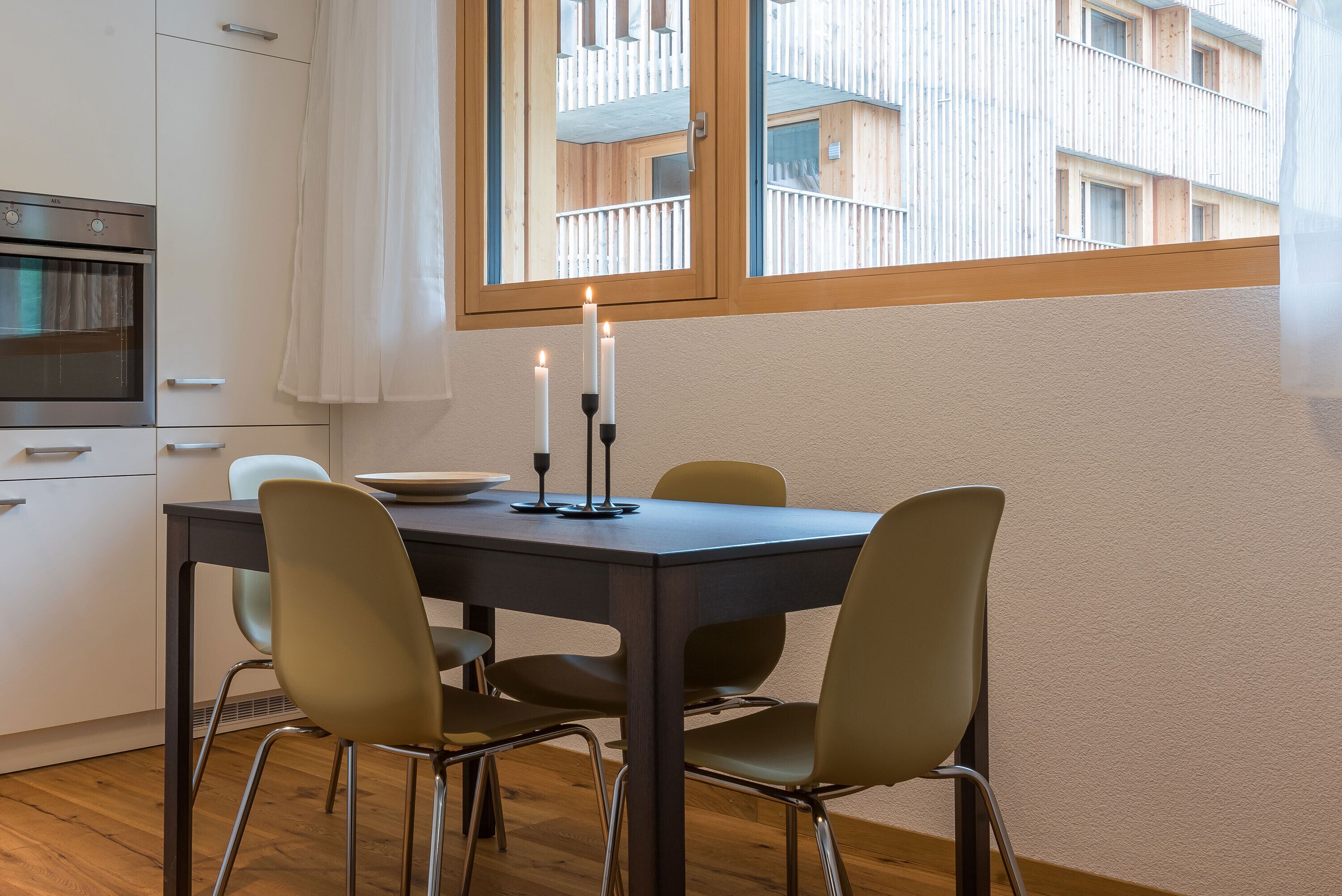 Una cocina moderna con una mesa de comedor, cuatro sillas y un ventanal con vista a un edificio.