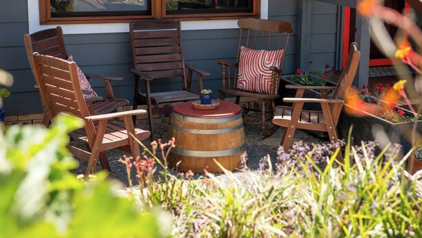 Een terras met houten stoelen en een rond tuintafel, omringd door planten en bloemen.