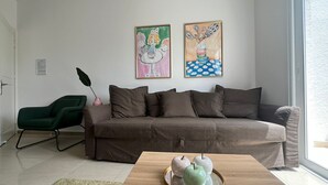 A modern living room with a brown sofa, a green chair, and a wooden coffee table with decorative apples. There are two framed artworks on the wall. - Cosy 1/bdr central apart near the beach

 (Paphos)
