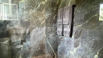A modern bathroom with a marble wall, a wooden floor, and a towel rack.