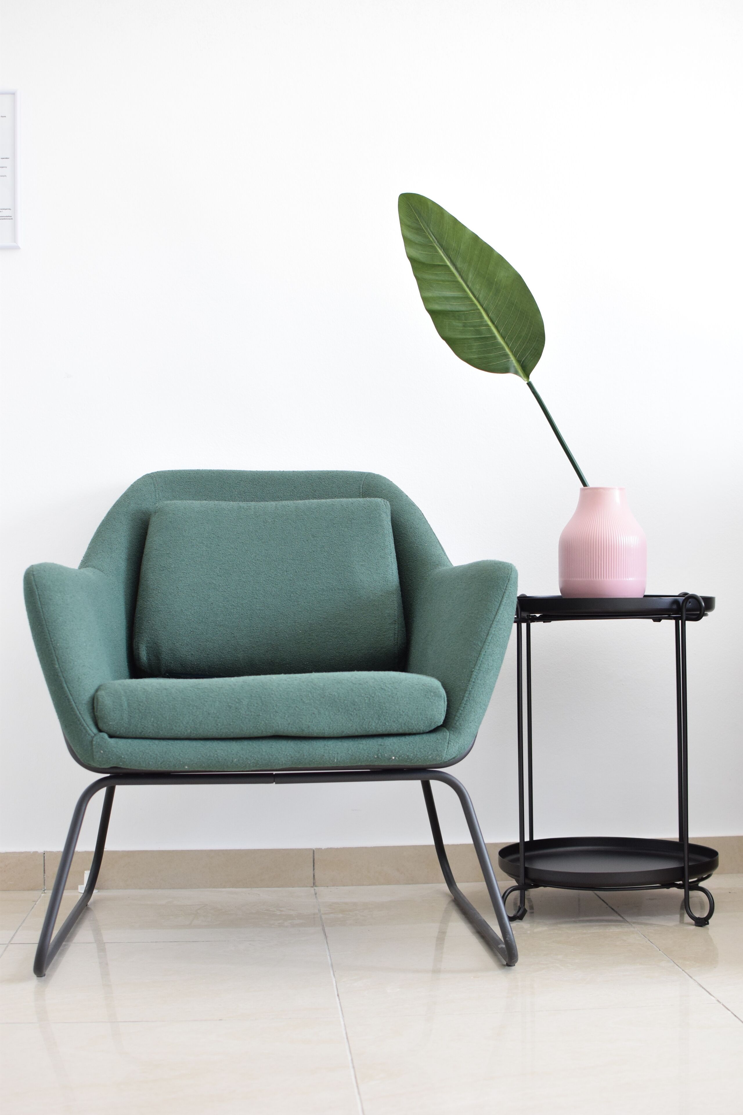 En turkis lænestol med pude, et sort metaltablet og en lyserød vase med en grøn plante.