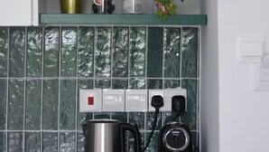 A kitchen with a green shelf holding a potted plant, two purple vases, and jars. There are two coffee makers and a kettle on the counter. - Cosy 1/bdr central apart near the beach

 (Paphos)