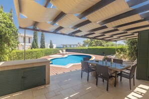Ein überdachter Außenbereich mit Pool, Sitzgelegenheiten und Meerblick.