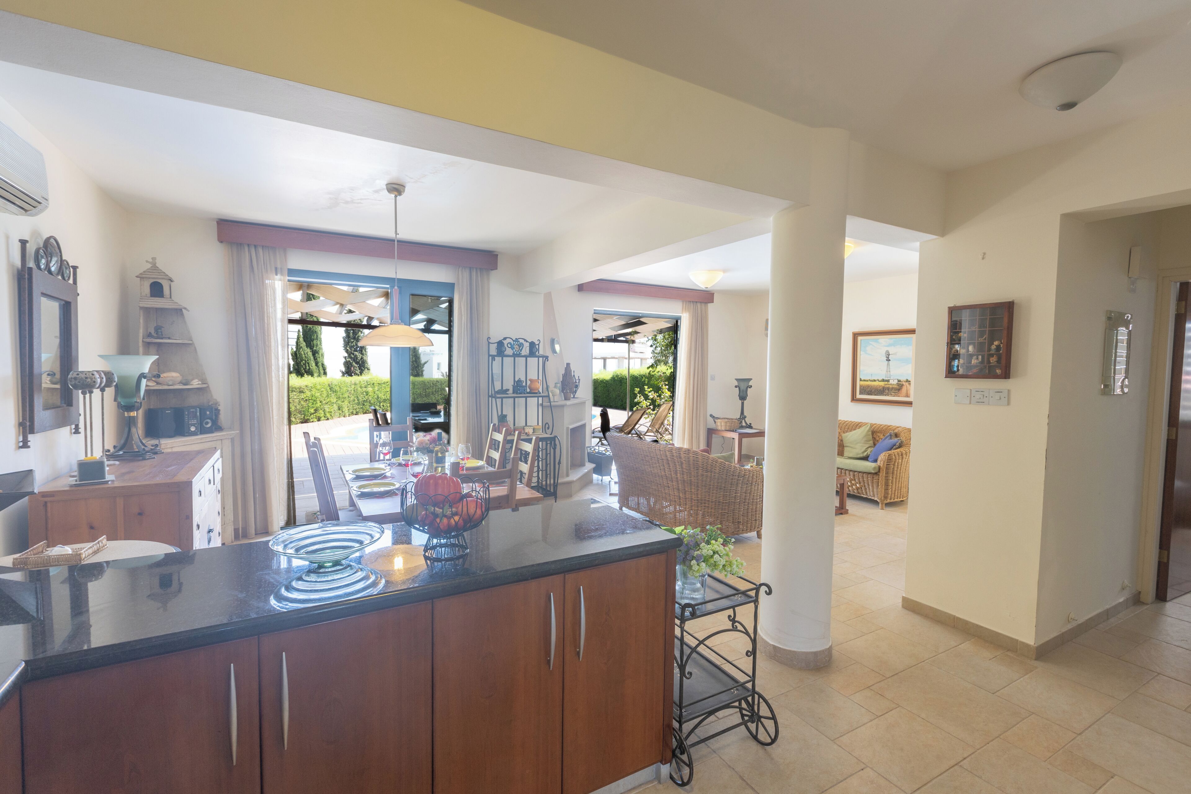 A spacious kitchen with a central island, a dining area with a table and chairs, and a view of the garden through an open door.