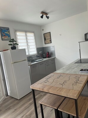 Une cuisine moderne avec un réfrigérateur blanc, des armoires grises, une table en bois ornée de messages écrits à la main, une plante en pot et une fenêtre avec des stores.