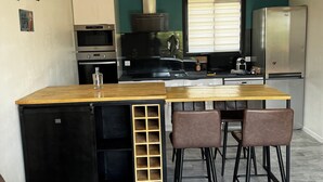 Una cocina compacta con una isla central, taburetes de bar, un refrigerador y un microondas.