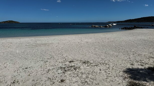 Una playa con agua azul cristalina, una orilla arenosa y una pequeña isla a lo lejos.