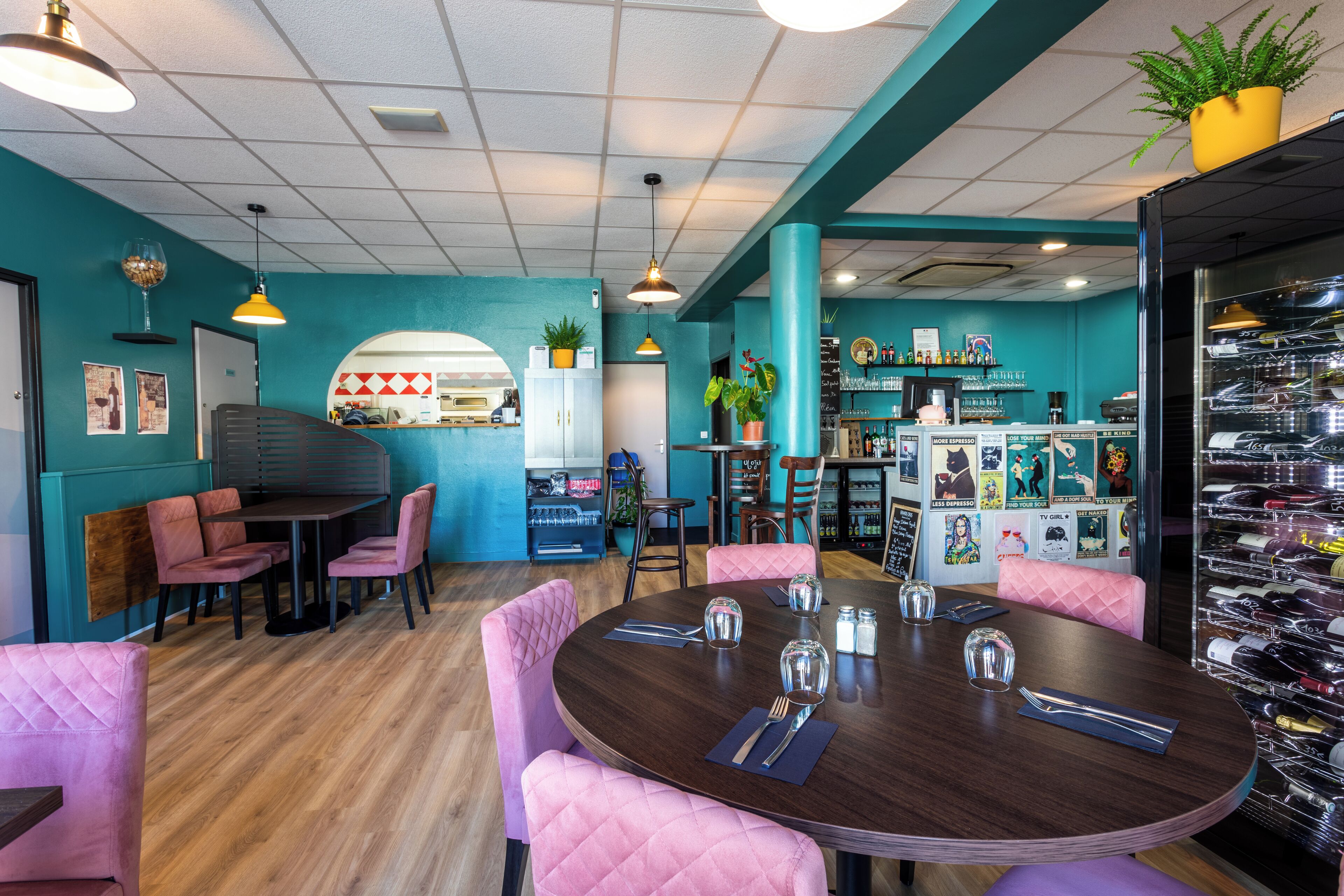 Un restaurante con paredes verde azulado, suelo de madera, sillas tapizadas en rosa y una estantería para vinos.