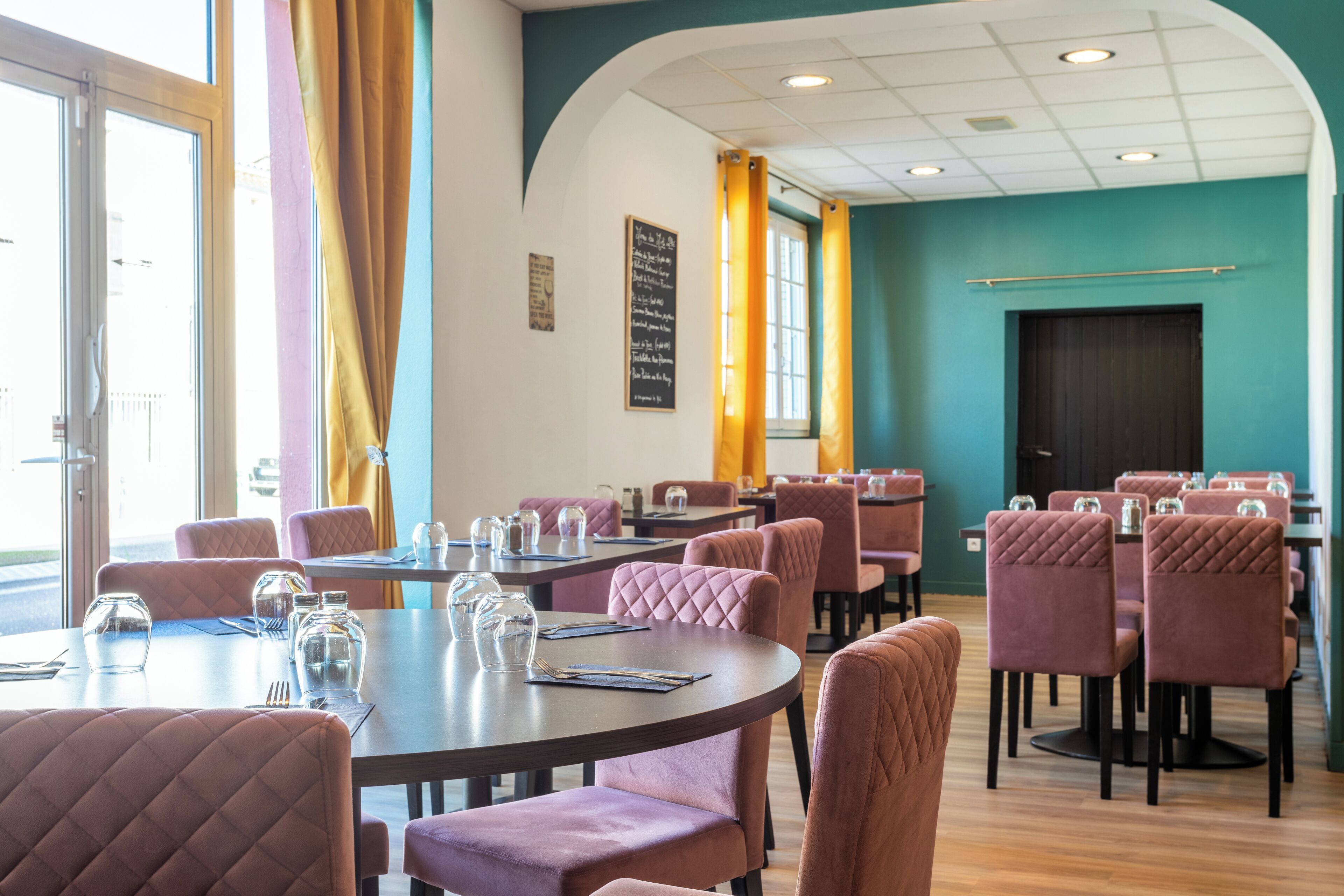 Un restaurant avec des tables rondes et des chaises rembourrées, un mur d’accent de couleur turquoise et un menu écrit à la craie.