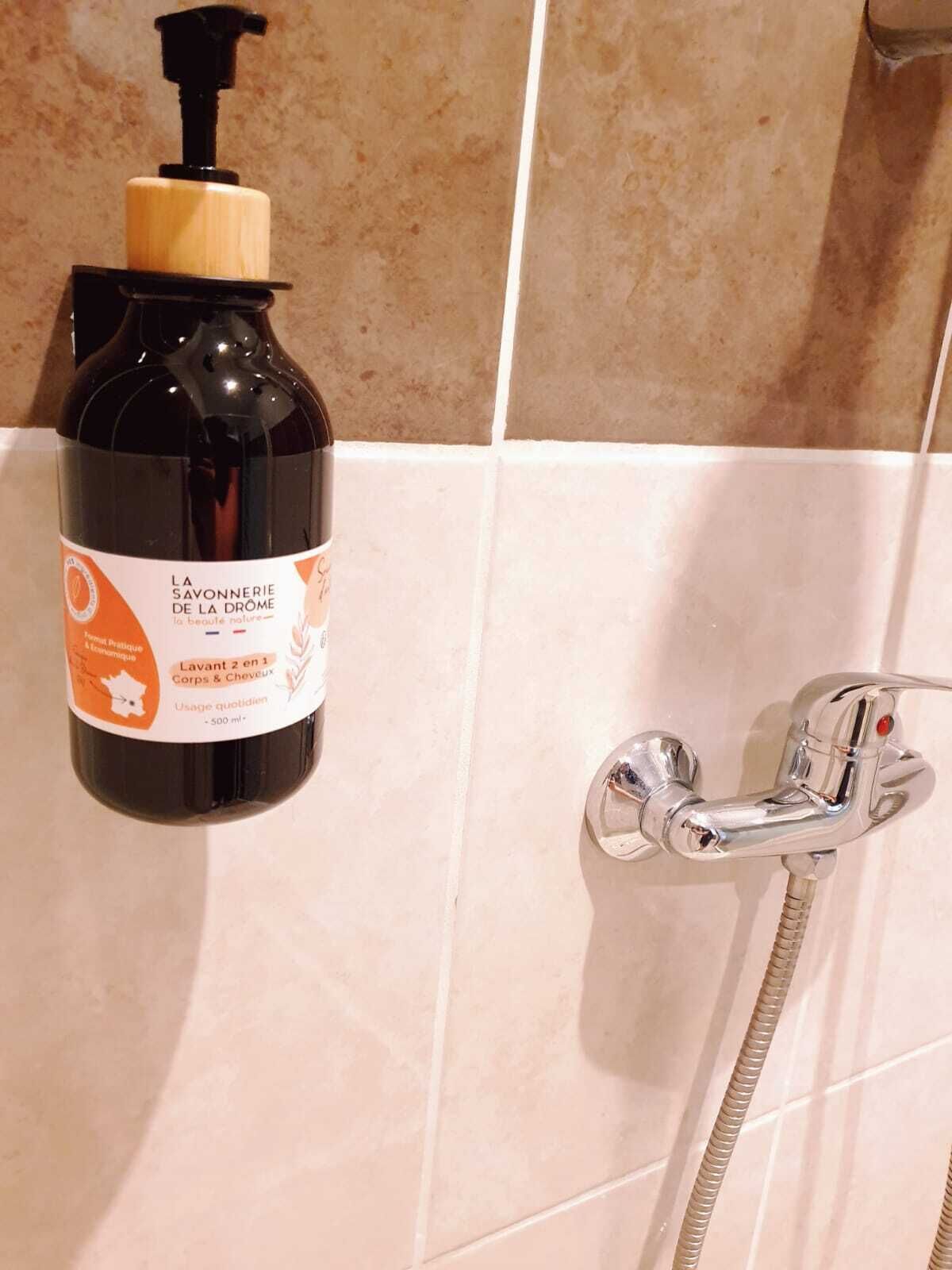 Un baño con ducha y una botella de jabón en la pared.