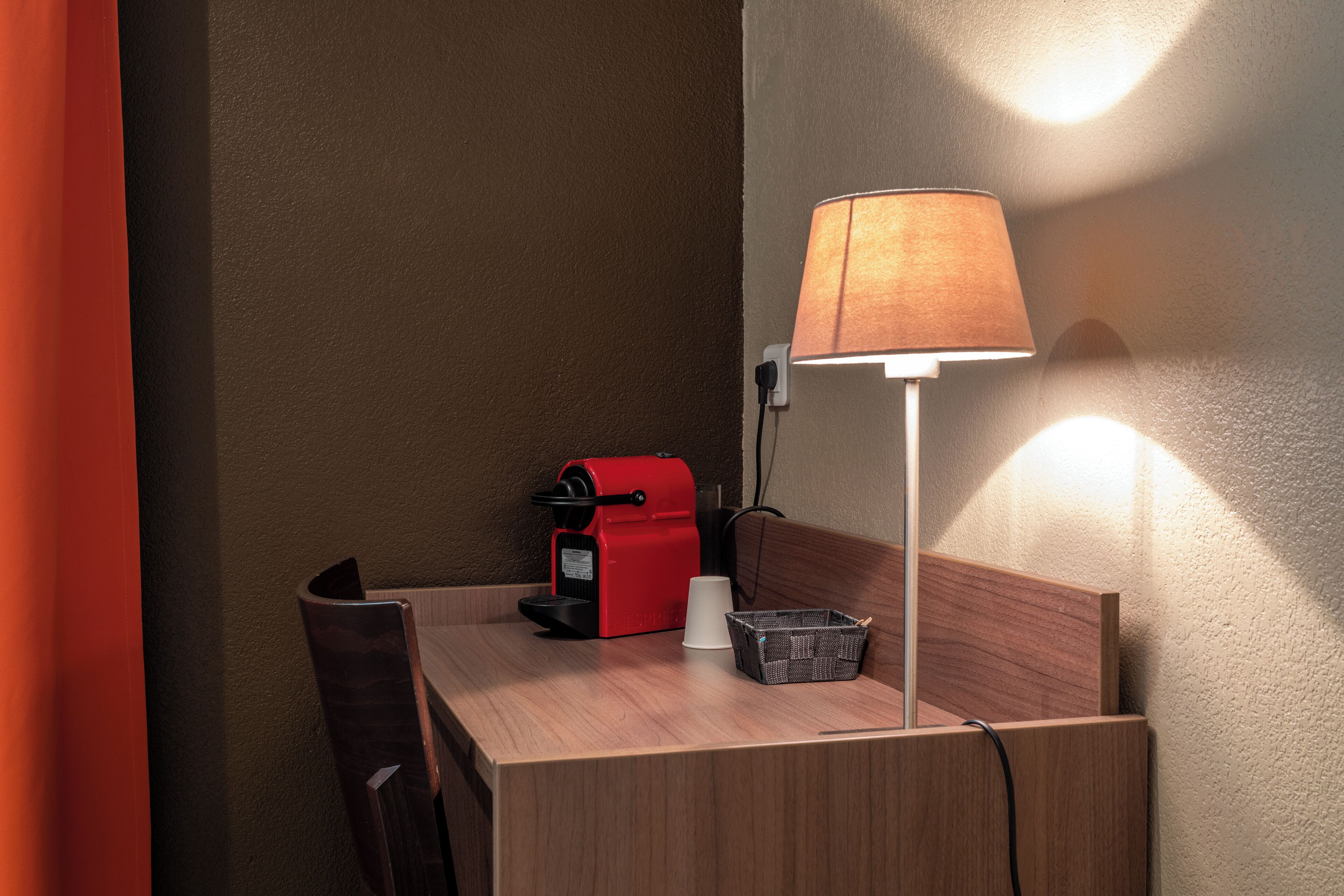 A small wooden table with a red coffee maker, a white cup, and a basket.