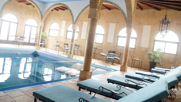 An indoor swimming pool with lounge chairs, arched columns, and large windows. - Hotel Balneario de Marmolejo (Marmolejo)