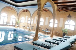 Une piscine intérieure dotée de chaises longues, de colonnes en arc de cercle et de grandes fenêtres.