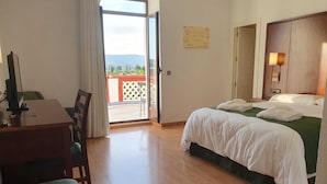 A hotel room with a desk, a bed with white linens, a view through a glass door, and a wall-mounted lamp. - Hotel Balneario de Marmolejo (Marmolejo)