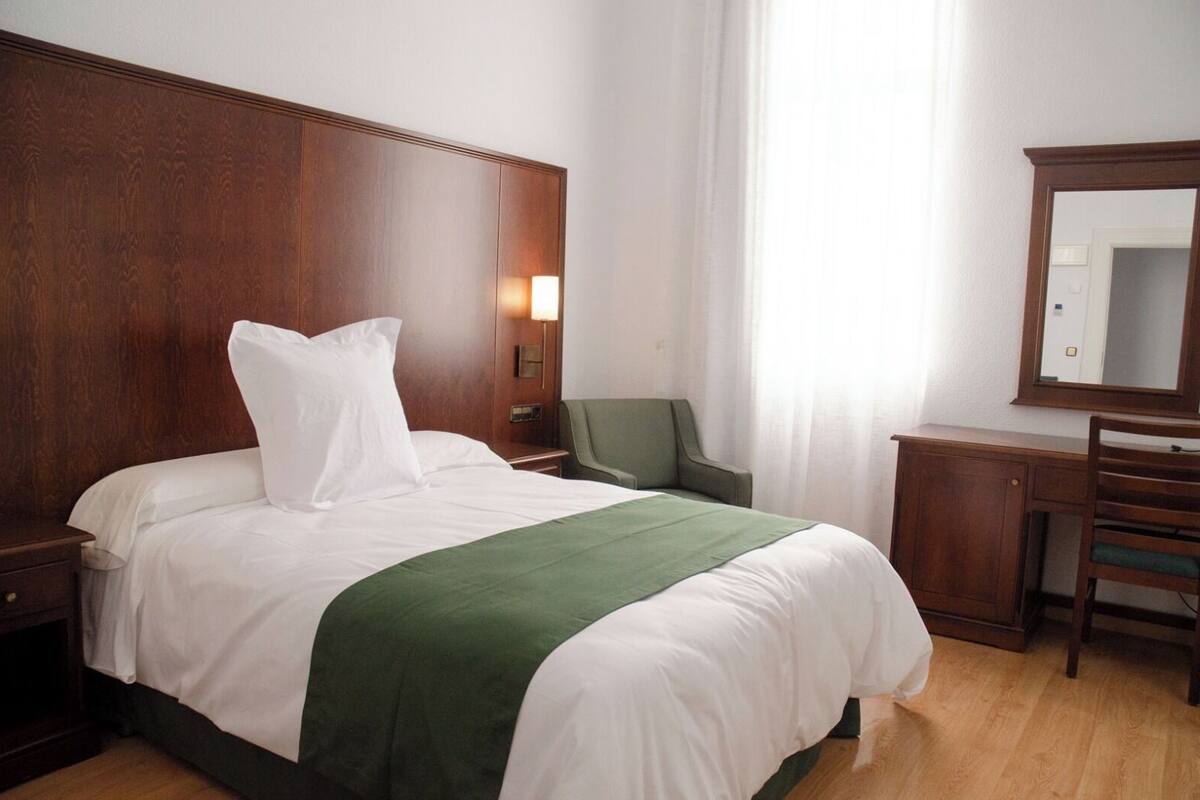 Una habitación de hotel con una cama grande, un escritorio, una silla y un espejo.